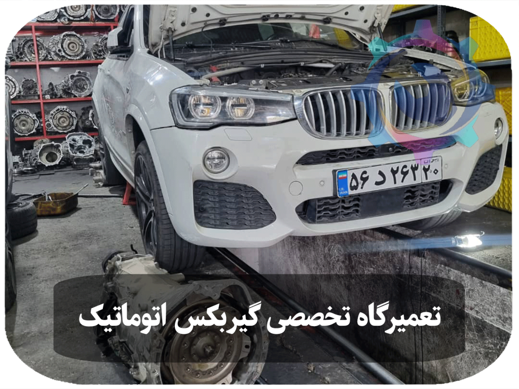 خودروی BMW X4 سفید رنگ که در حال تعمیر گیربکس اتوماتیک در تعمیرگاه تخصصی تویوکارا است. گیربکس جدا شده و در کنار خودرو قرار دارد، در حالی که خودرو روی بالابر قرار گرفته است.